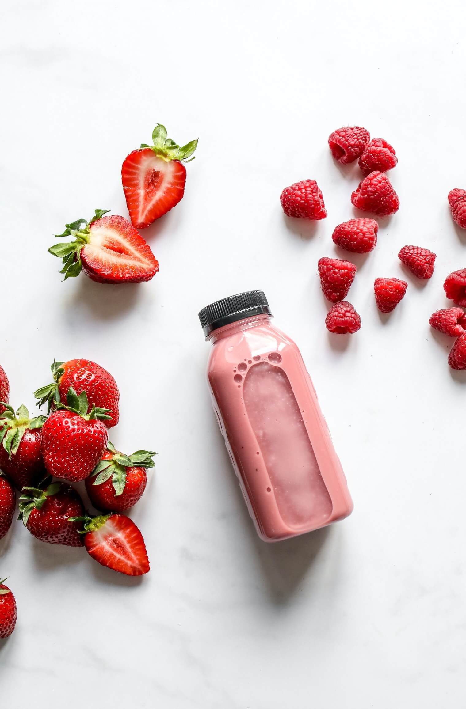 Smoothie with strawberries and raspberries besides it.