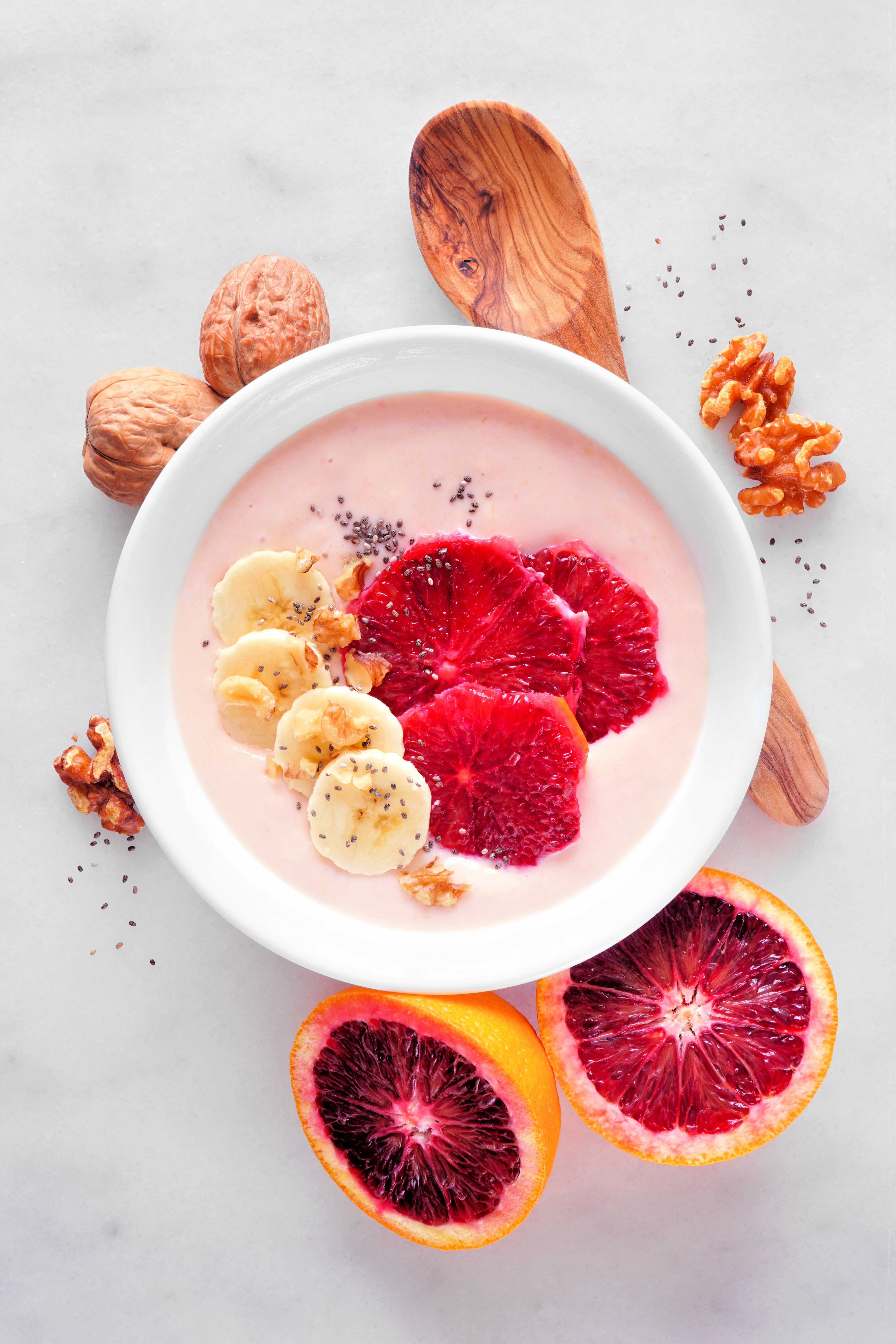 Healthy blood orange and banana smoothie bowl with walnuts and chia seeds. Top view table scene on a bright background.