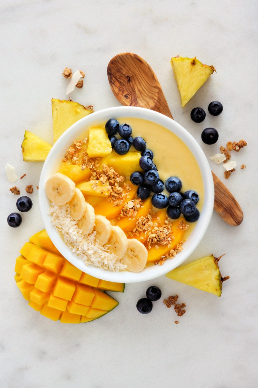  A pineapple, mango smoothie bowl with coconut, bananas, blueberries and granola. Above view scene on a bright background.