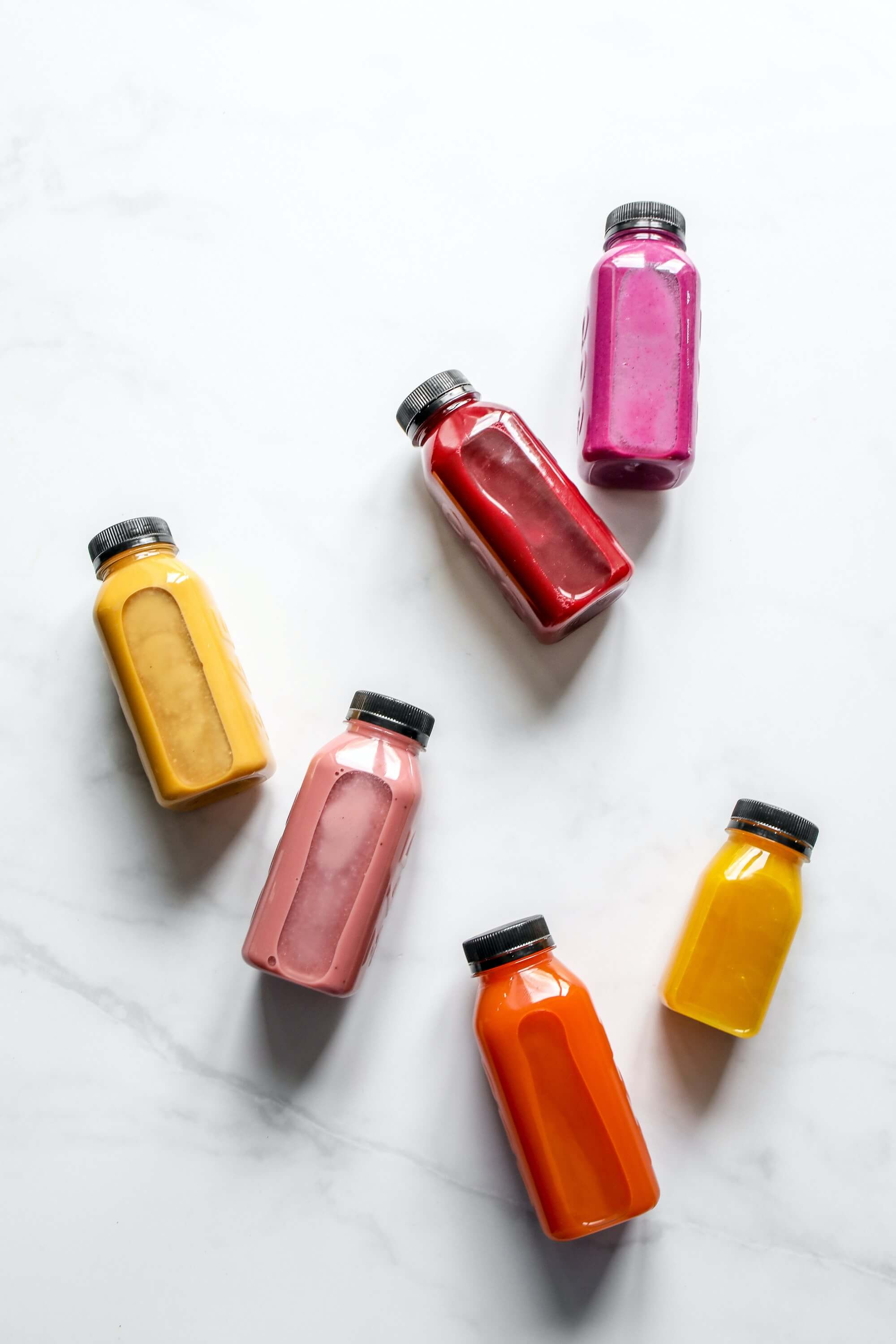 Different colored smoothie bottles on a white granite background.